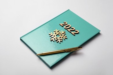 Photo of Turquoise planner, pen, wooden numbers and snowflake on white background. 2022 New Year aims