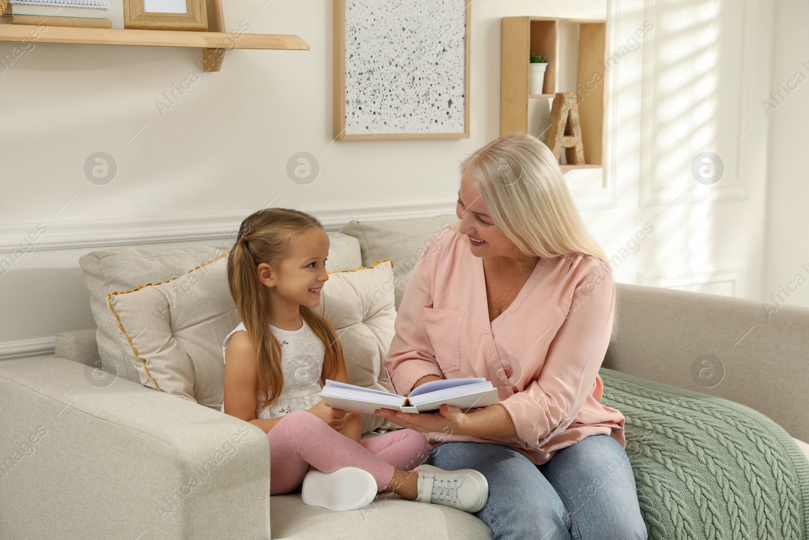 Photo of Happy grandmother with her granddaughter reading book together at home