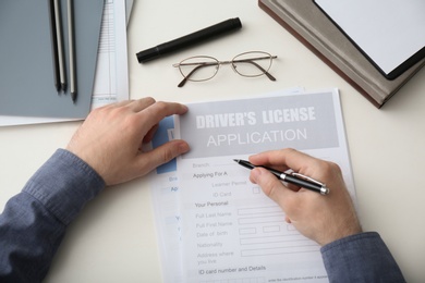 Photo of Man filling in driver's license application form at white table, top view