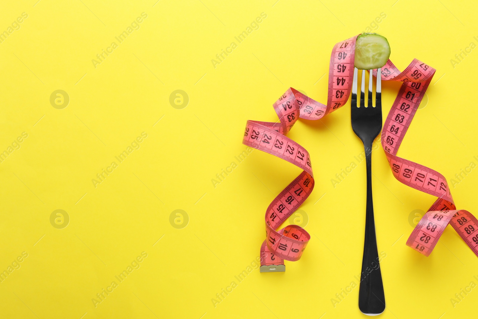 Photo of Fork with cucumber and measuring tape on yellow background, flat lay and space for text. Diet concept