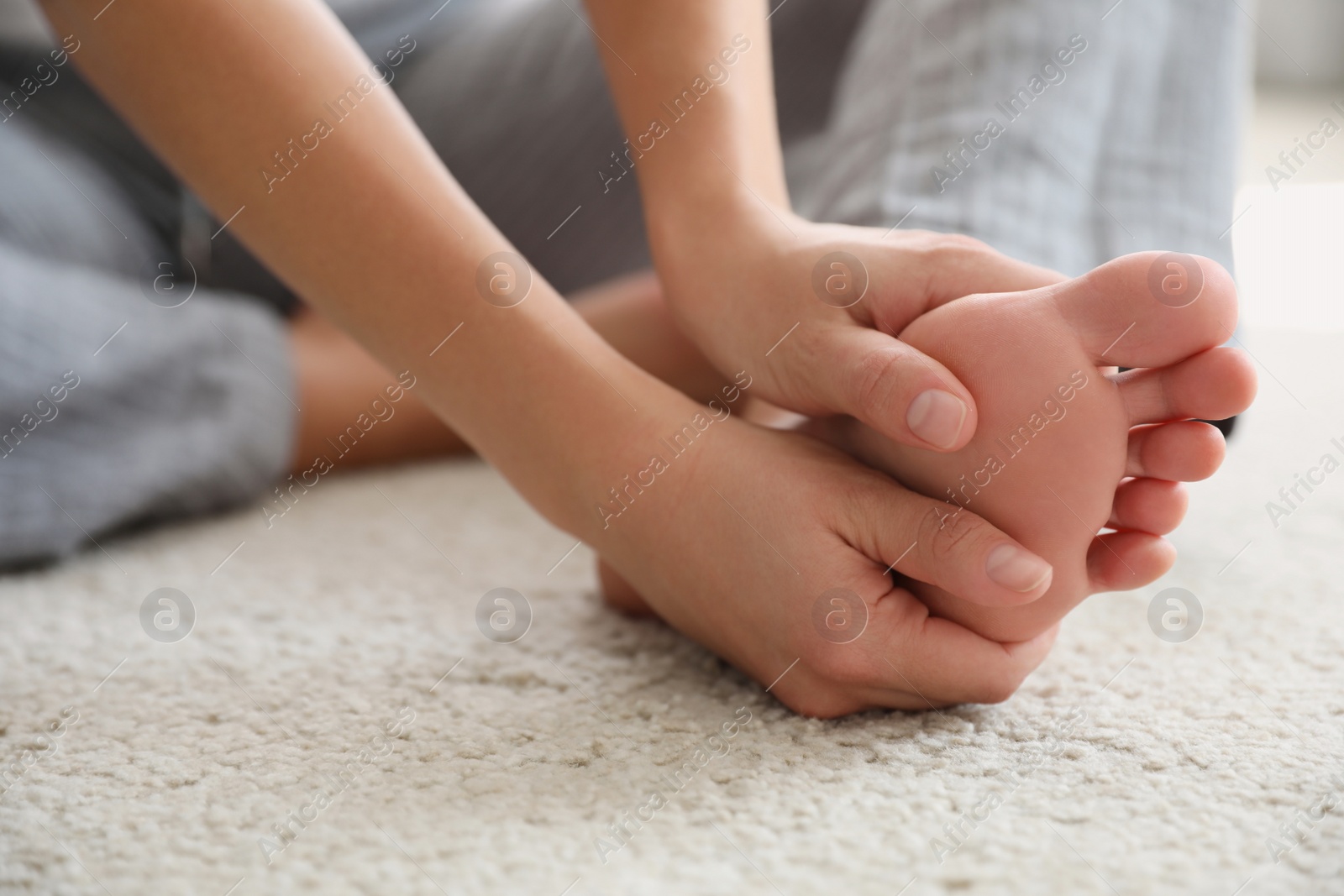 Photo of Young woman suffering from pain in foot on floor, closeup