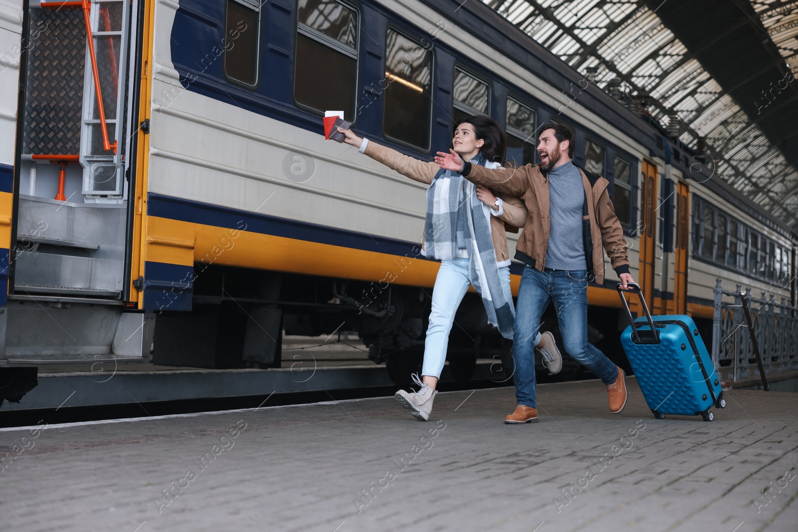 Photo of Being late. Worried couple with suitcase running towards train at station