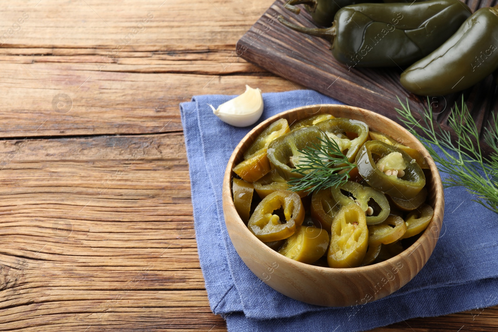 Photo of Bowl with slices of pickled green jalapeno peppers on wooden table, space for text