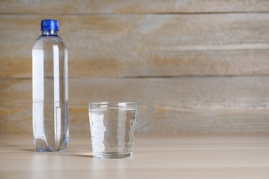 Photo of Glass and plastic bottle with water on table against wooden background, space for text