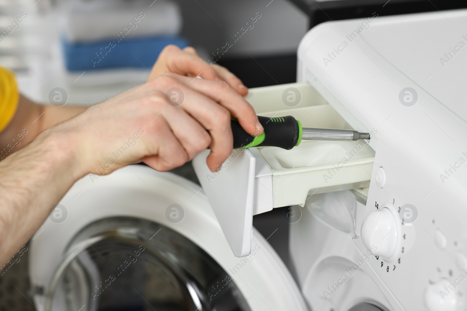 Photo of Plumber with screwdriver repairing washing machine indoors, closeup