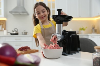Photo of Little girl using modern meat grinder in kitchen