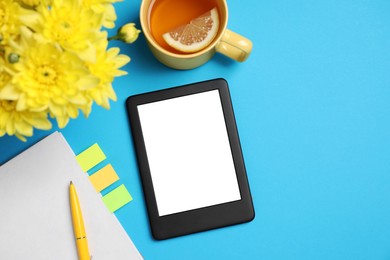 E-book reader with notebook, cup of tea and flowers on light blue background, flat lay. Space for text