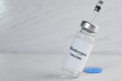 Filling syringe with monkeypox vaccine from vial at white wooden table, space for text