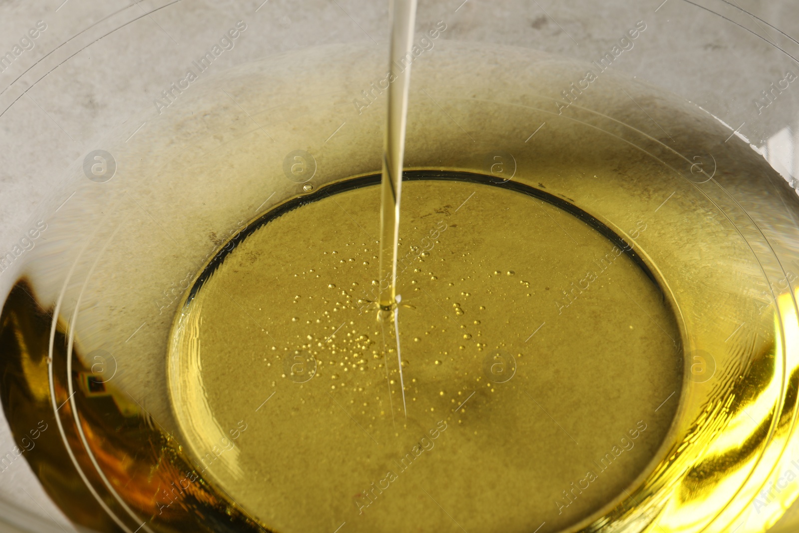 Photo of Pouring cooking oil into glass bowl, closeup