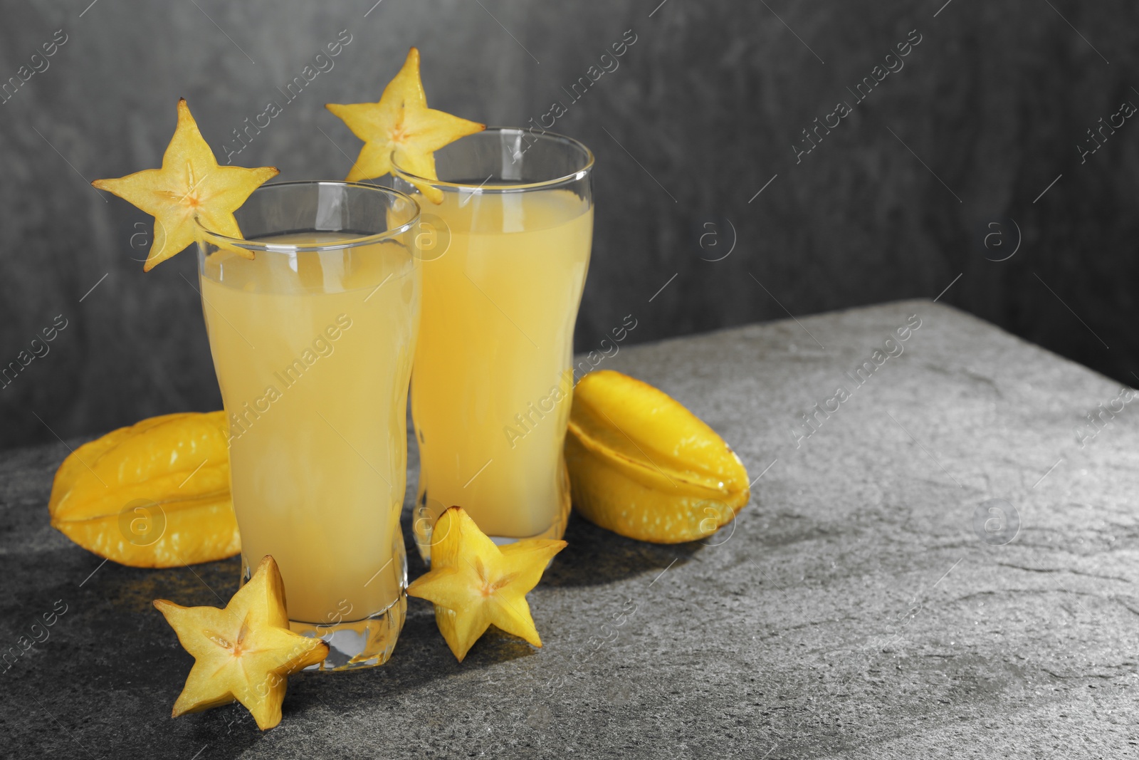 Photo of Delicious carambola juice and fresh fruits on grey table. Space for text