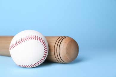 Photo of Wooden baseball bat and ball on light blue background, space for text. Sports equipment