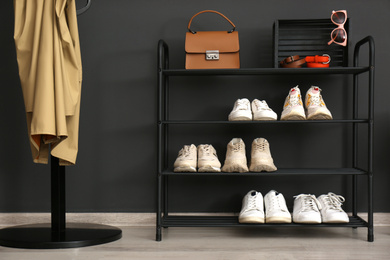Shelving rack with stylish shoes and accessories near black wall at home. Idea for hallway interior design