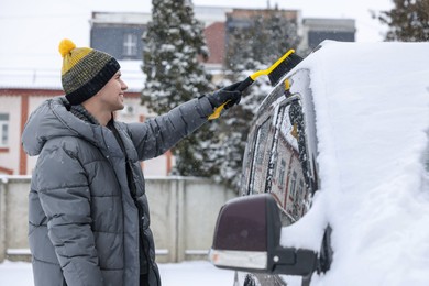 Man cleaning snow from car with brush outdoors