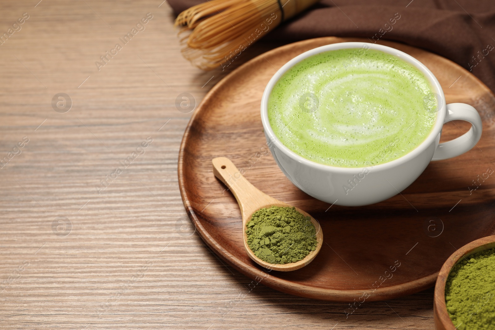 Photo of Cup of fresh matcha latte and powder on wooden table. Space for text