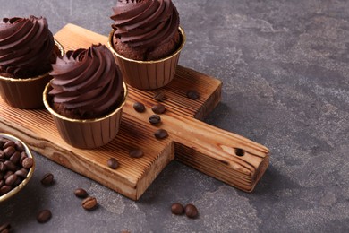 Photo of Delicious chocolate cupcakes and coffee beans on grey textured table, closeup. Space for text