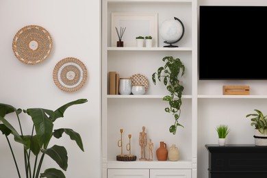 Stylish shelves with decorative elements and houseplants near white wall. Interior design