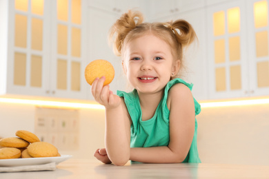 Photo of Cute little girl eating cookies in kitchen