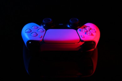 Photo of Wireless game controller on black mirror surface in neon lights