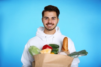 Young man holding paper bag with products on color background. Food delivery service