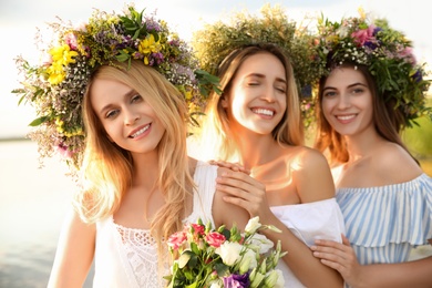 Photo of Young women wearing wreaths made of beautiful flowers near river on sunny day