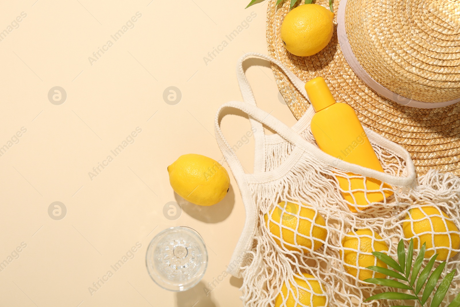 Photo of Fresh lemons, beach accessories in string bag and glass of drink on beige background, flat lay. Space for text