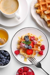 Photo of Delicious Belgian waffles with fresh berries and honey served on white table, flat lay