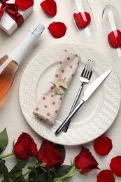 Photo of Beautiful table setting with gift box and rose petals on white wooden table for romantic dinner, flat lay