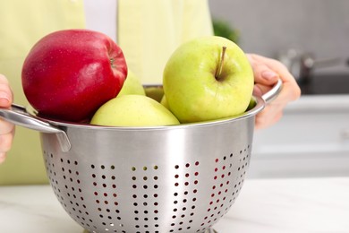 Photo of Woman holding colander with fresh apples at table indoors, closeup