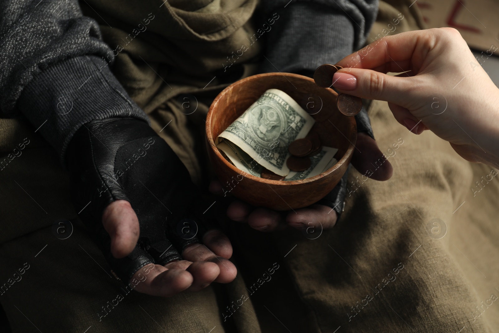 Photo of Woman giving coin to poor homeless man with bowl of donations, closeup