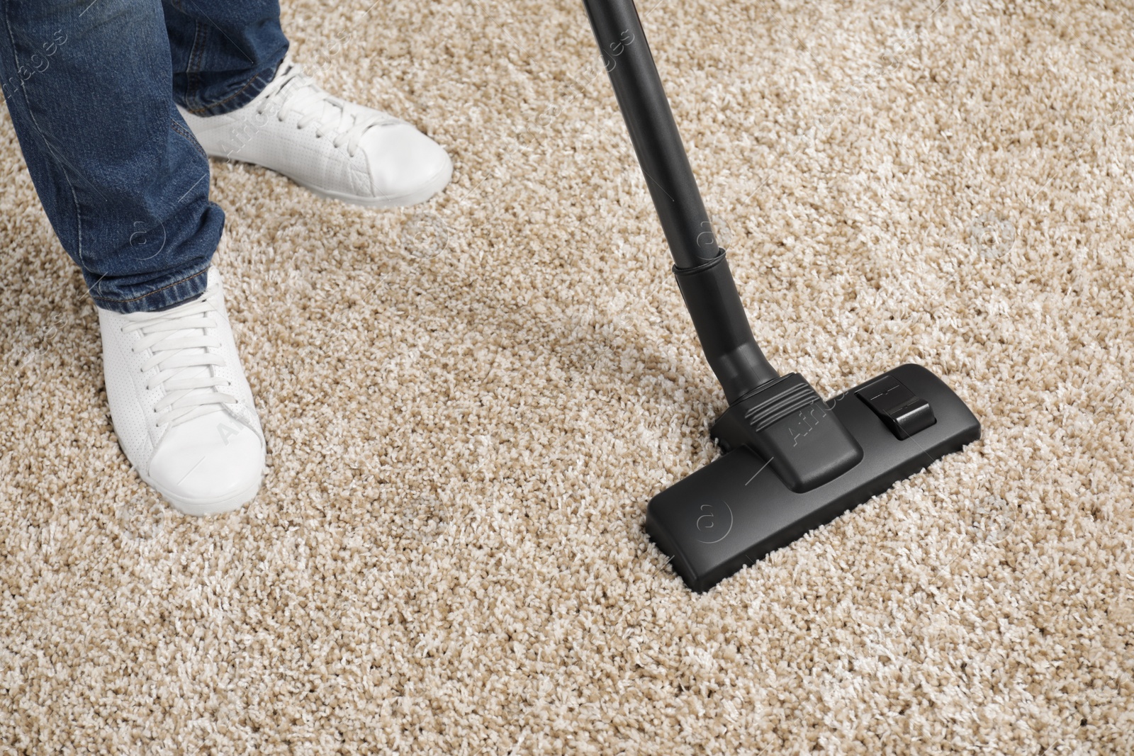 Photo of Man cleaning carpet with vacuum cleaner at home, closeup