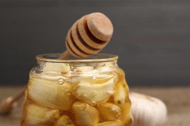 Photo of Honey with garlic in glass jar and dipper on blurred background, closeup. Space for text