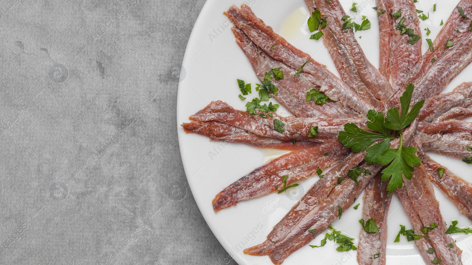 Photo of Plate with anchovy fillets and parsley on grey table, top view. Space for text