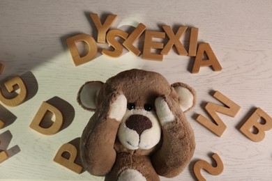 Photo of Word Dyslexia made of letters and teddy bear on light wooden table, flat lay