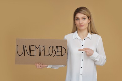Photo of Woman holding sign with word Unemployed on beige background