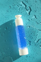 Bottle of cosmetic product on wet turquoise background, top view