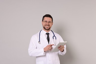 Portrait of smiling doctor with tablet on light grey background