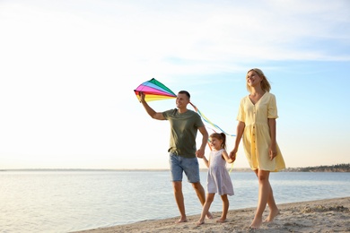 Photo of Happy parents with their child playing with kite on beach, space for text. Spending time in nature