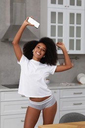 Photo of Beautiful woman in stylish underwear and t-shirt listening to music through wireless earphones indoors