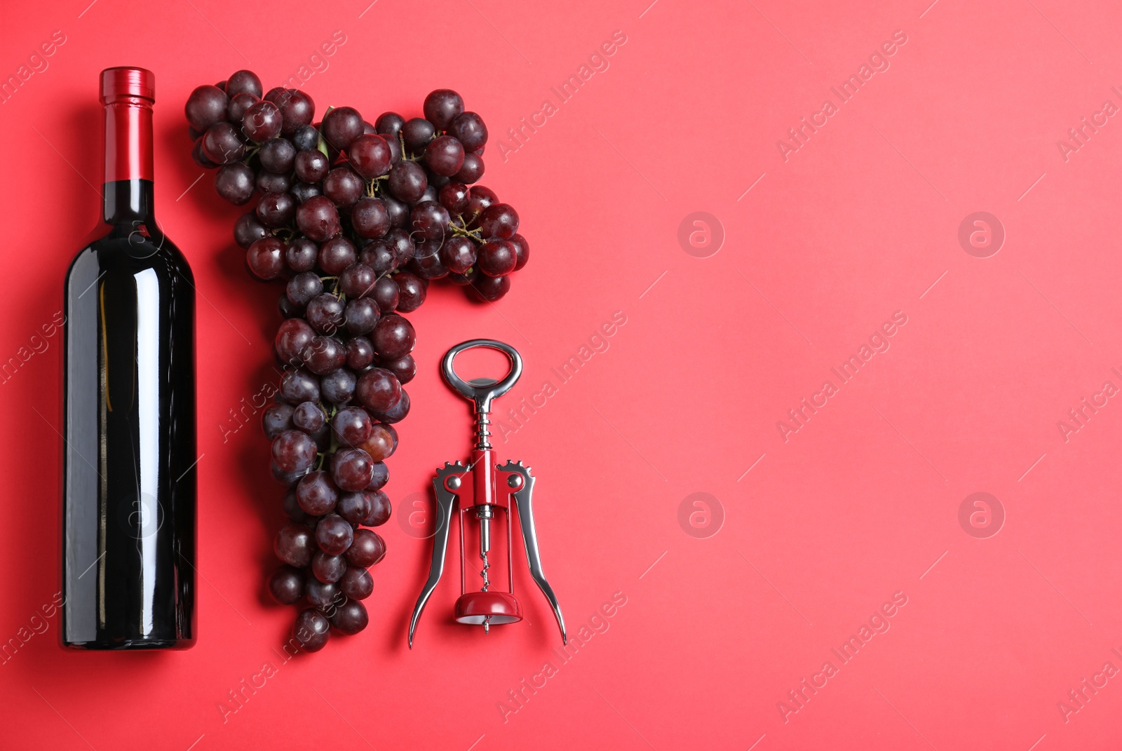 Photo of Fresh ripe juicy grapes and bottle of wine on red background, flat lay. Space for text