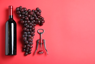 Fresh ripe juicy grapes and bottle of wine on red background, flat lay. Space for text