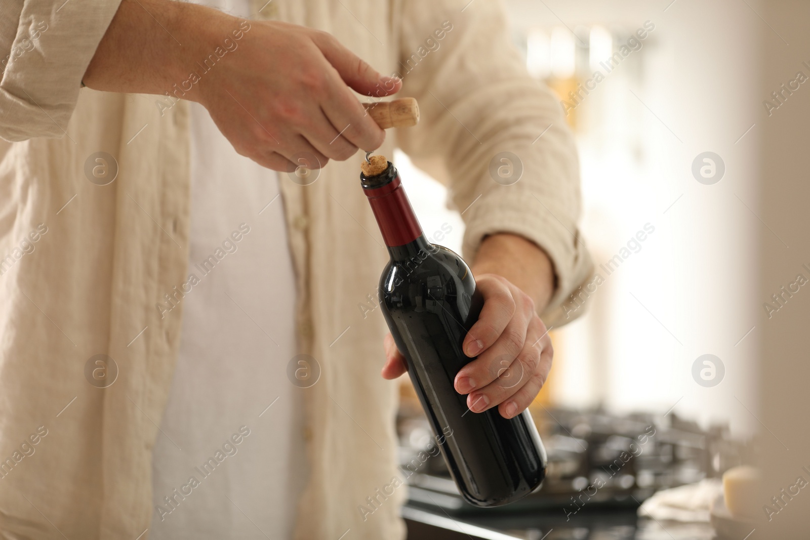 Photo of Man opening wine bottle with corkscrew indoors, closeup