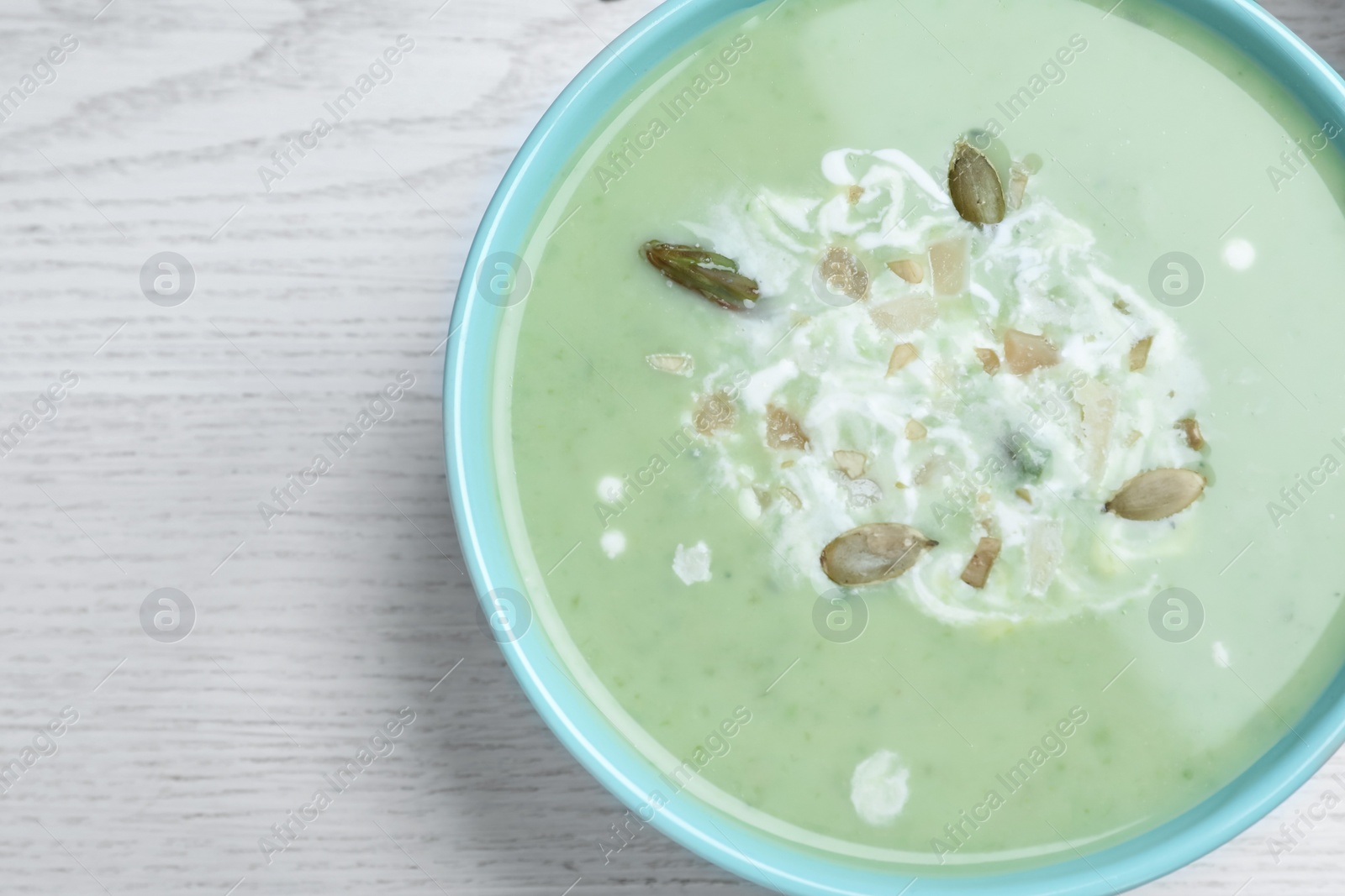 Photo of Bowl of delicious asparagus soup on white wooden table, top view. Space for text