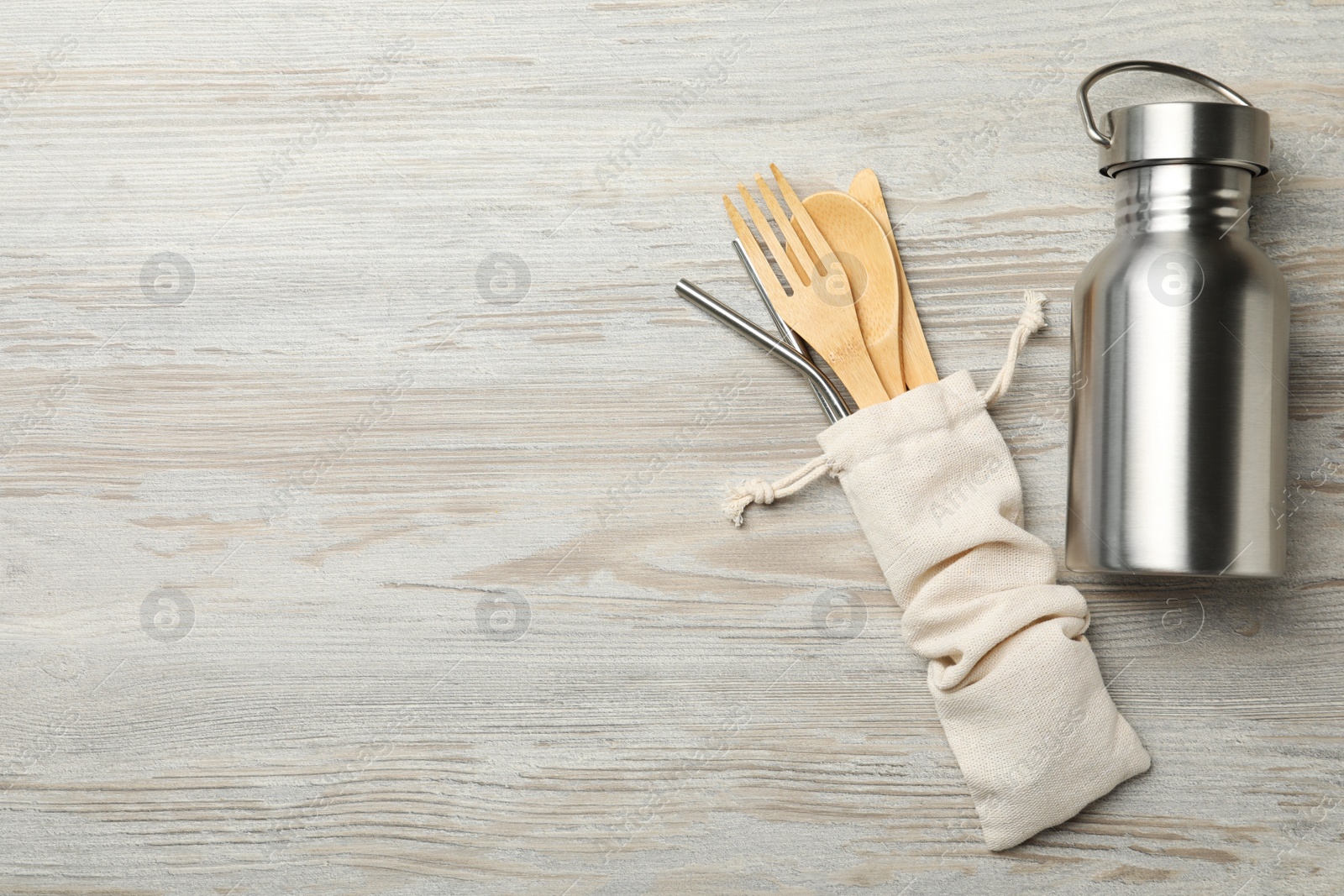 Photo of Metal bottle, straws and bamboo cutlery on wooden background, flat lay with space for text. Conscious consumption