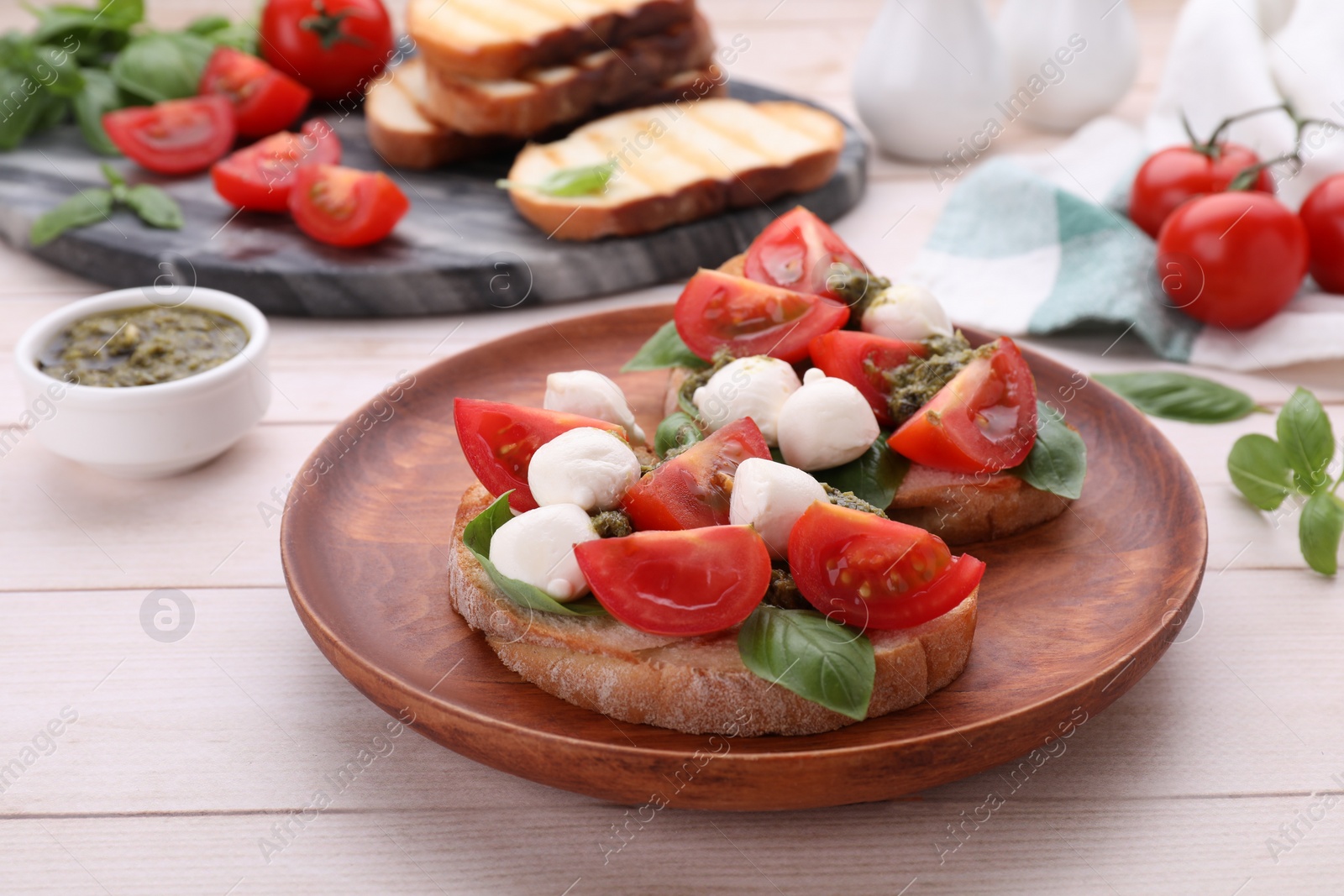 Photo of Delicious Caprese sandwiches with mozzarella, tomatoes, basil and pesto sauce on white wooden table