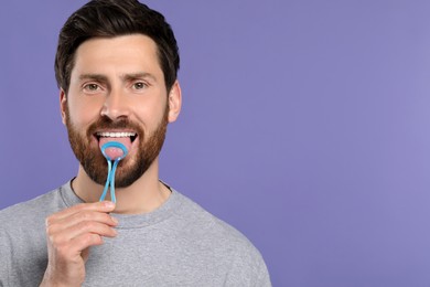 Happy man brushing his tongue with cleaner on violet background, space for text