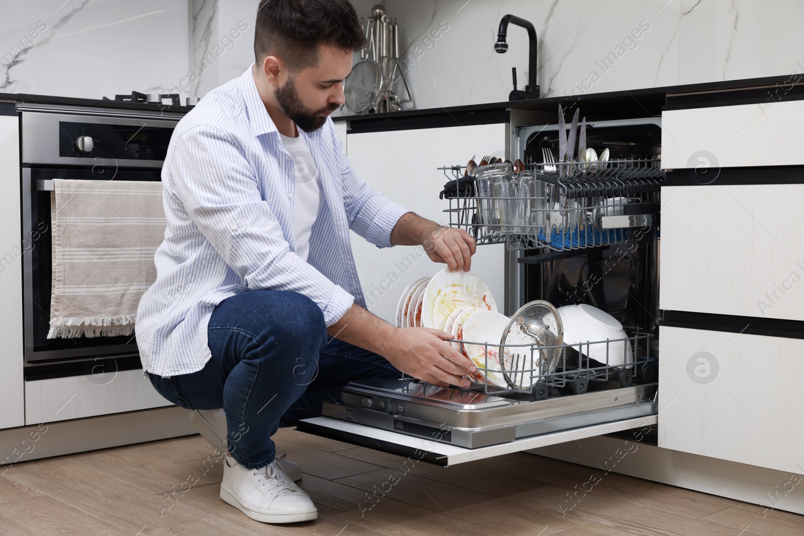 Photo of Man loading dishwasher with dirty plates indoors