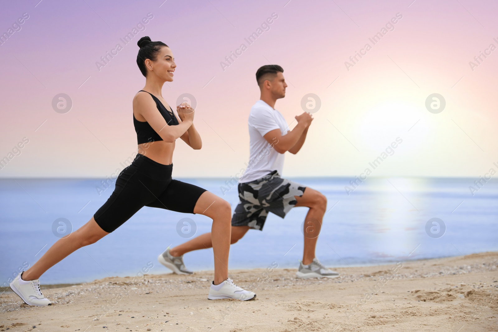Image of Couple doing yoga exercise together on beach at sunrise