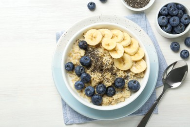 Photo of Tasty oatmeal with banana, blueberries and chia seeds served in bowl on white wooden table, flat lay