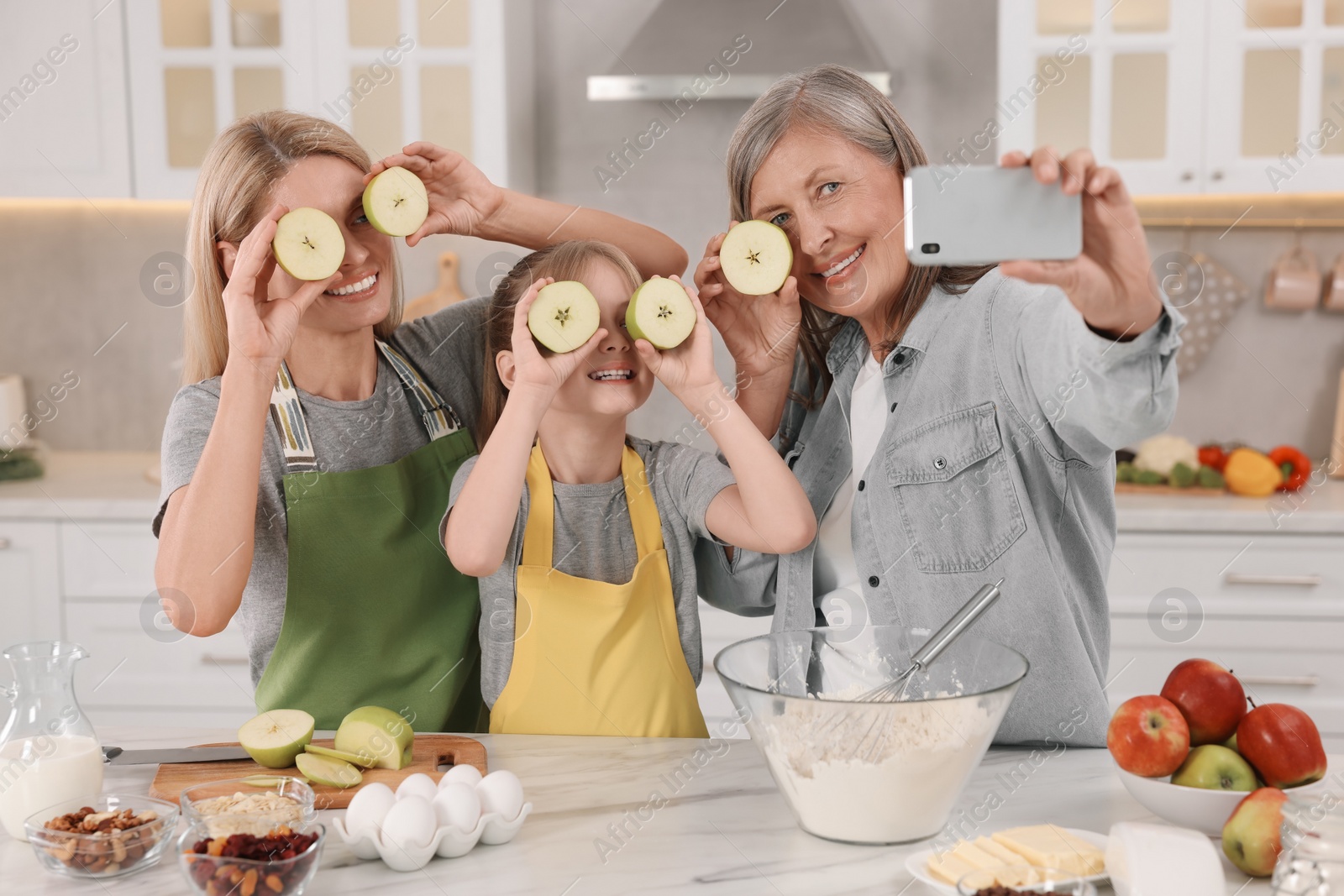 Photo of Three generations. Happy grandmother, her daughter and granddaughter taking selfie while cooking together in kitchen