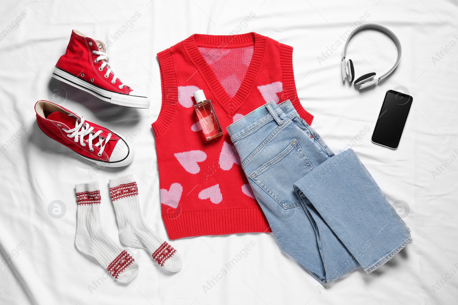 Photo of Pair of stylish red shoes, clothes and smartphone on white fabric, flat lay